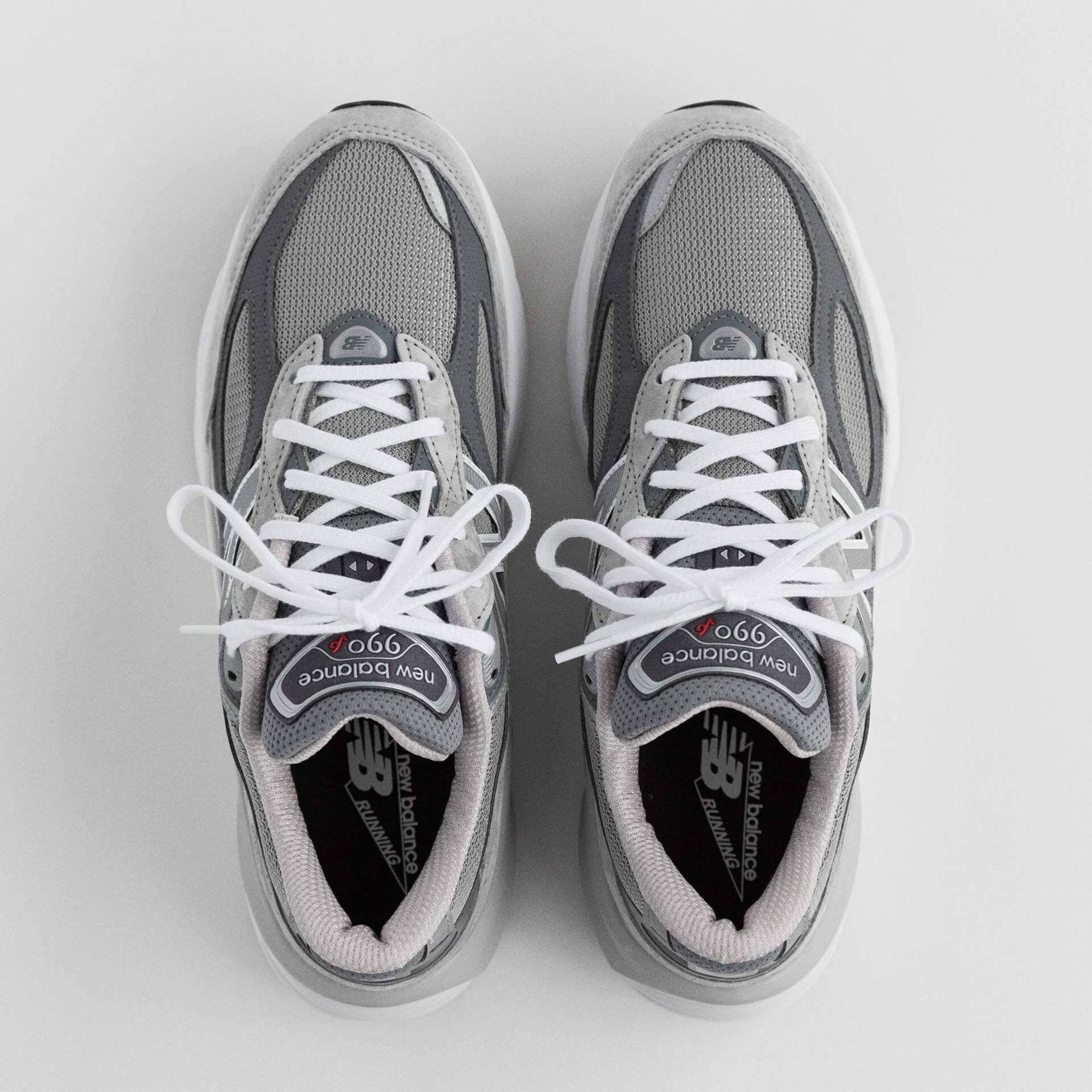 A top-down image of a pair of grey 990v6 sneakers on a grey studio backdrop. 
