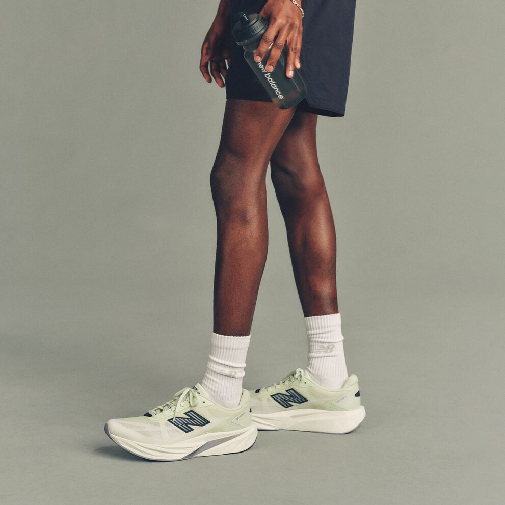 Studio image showing a person&rsquo;s lower body from mid-thigh down, standing against a smooth, light gray background.