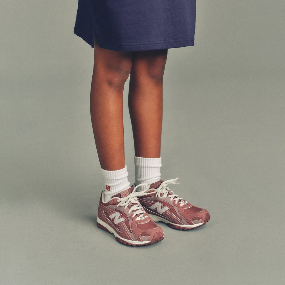 The child is wearing a navy top that extends to mid-thigh and white ribbed crew socks featuring a small red &ldquo;NB&rdquo; logo near the cuff
