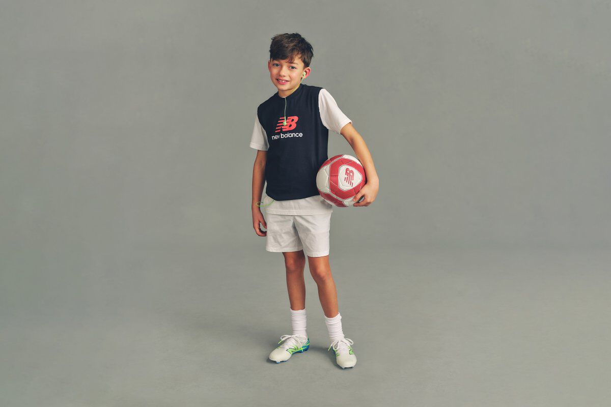 Close-up studio image of a child wearing a navy hooded sweatshirt with a &ldquo;New Balance Running&rdquo; logo printed on the chest.