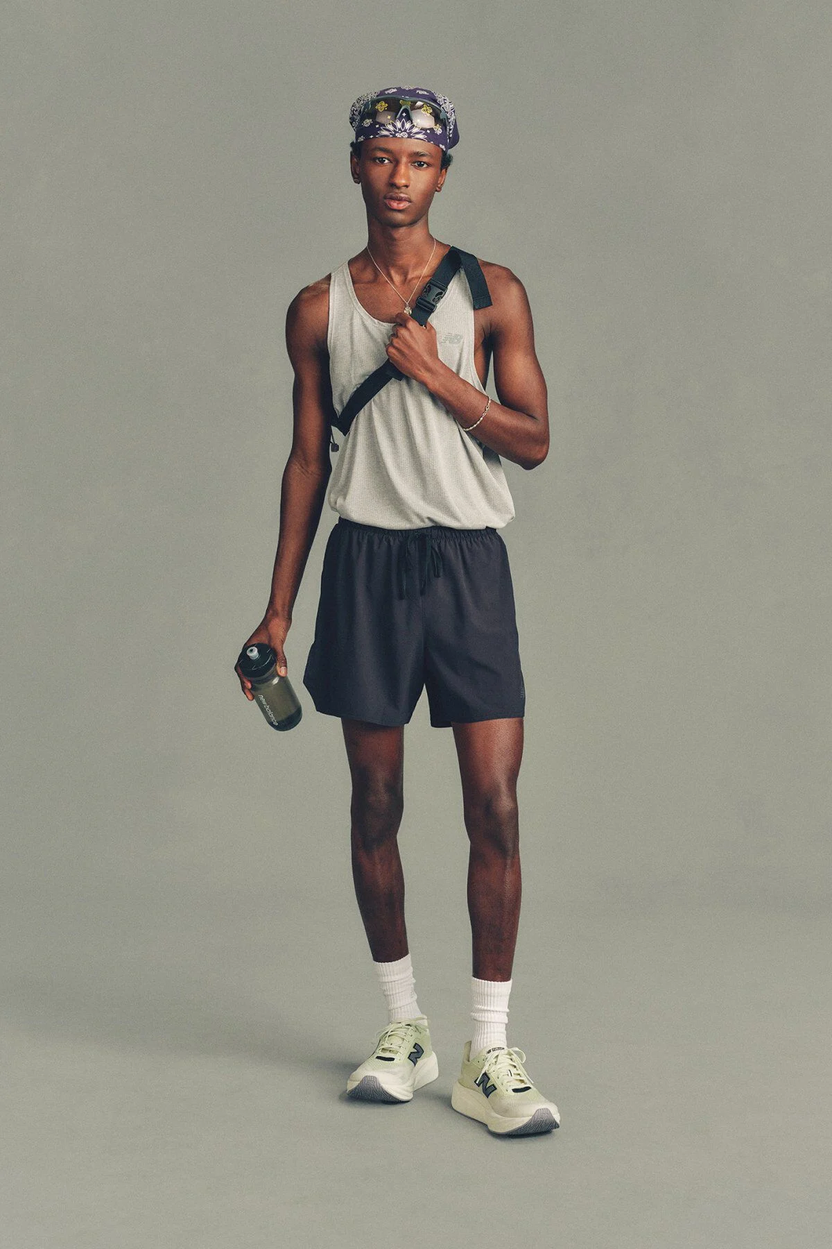 The person is wearing a light gray sleeveless athletic tank top and dark running shorts, paired with white crew socks and light-colored New Balance running shoes. 