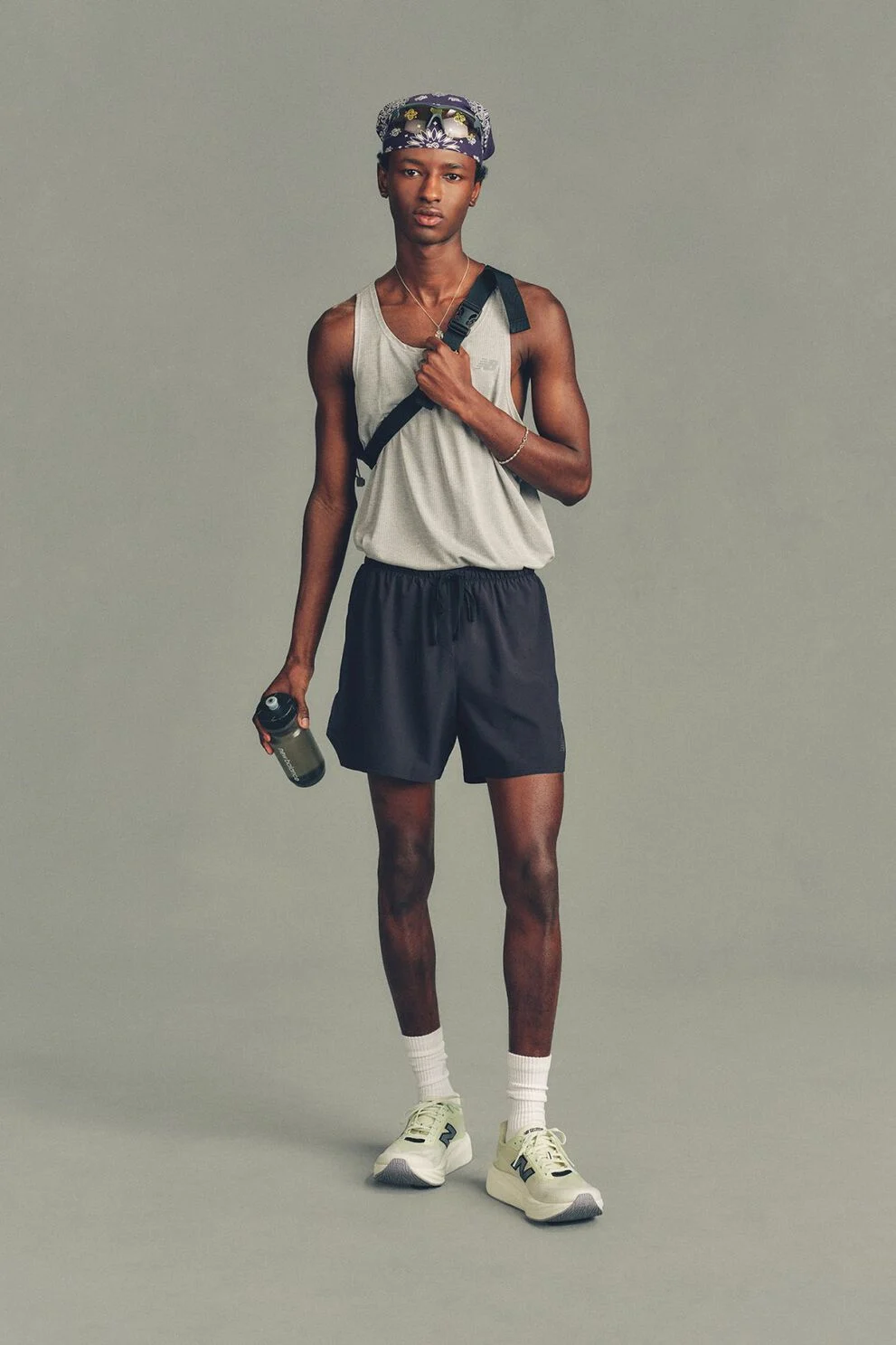 The person is wearing a light gray sleeveless athletic tank top and dark running shorts, paired with white crew socks and light-colored New Balance running shoes. 
