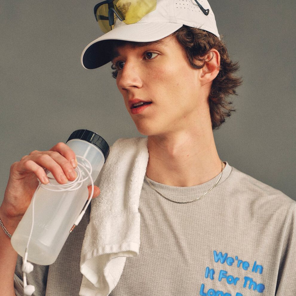 The person is wearing a light gray athletic T-shirt with blue text partially visible reading &ldquo;We&rsquo;re In It For The Long Run.&rdquo; 