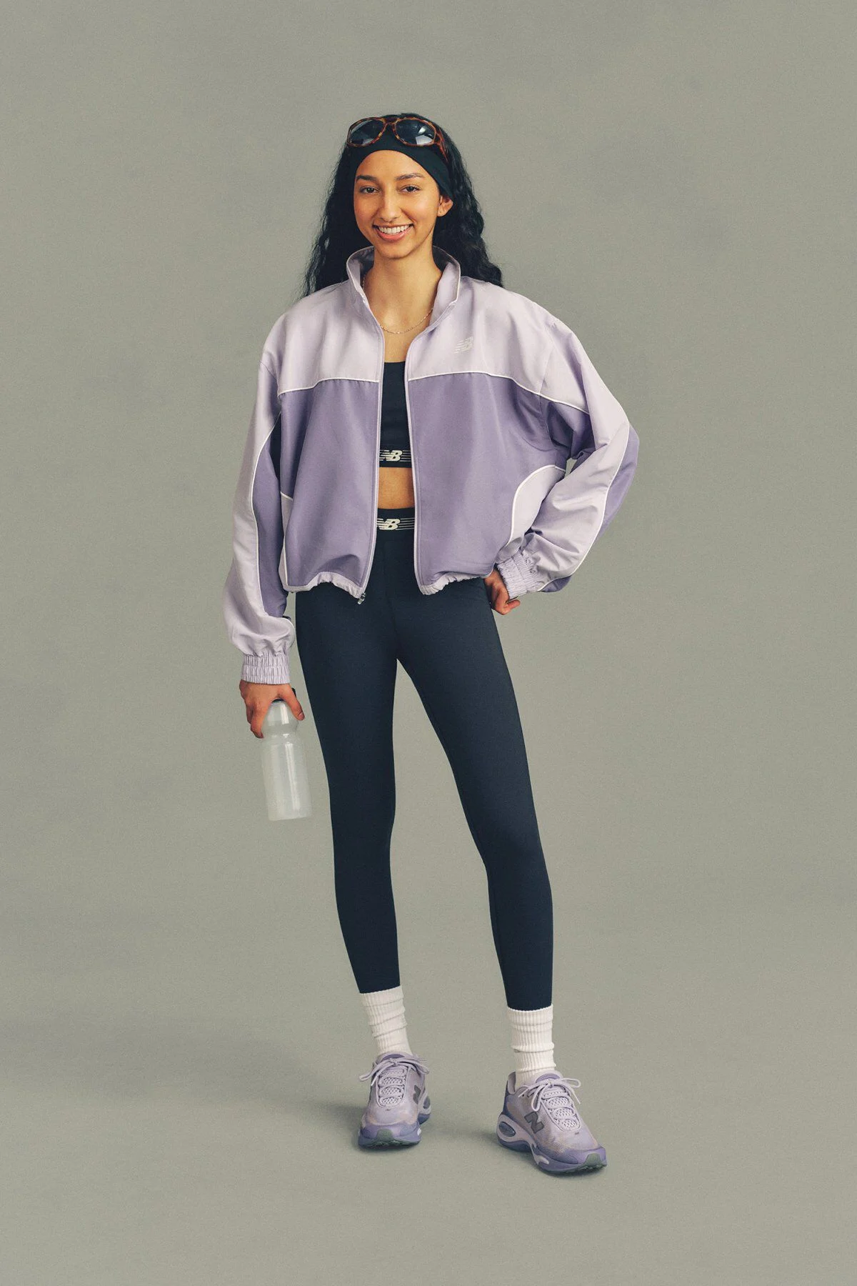 The person is wearing a lavender and light purple zip-up athletic jacket over a dark sports bra, paired with navy leggings. 