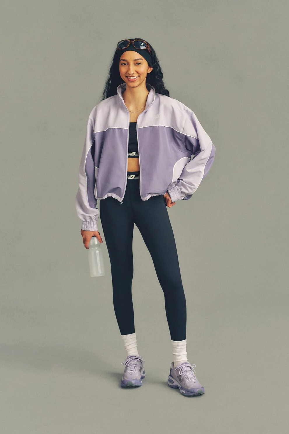 The person is wearing a lavender and light purple zip-up athletic jacket over a dark sports bra, paired with navy leggings. 