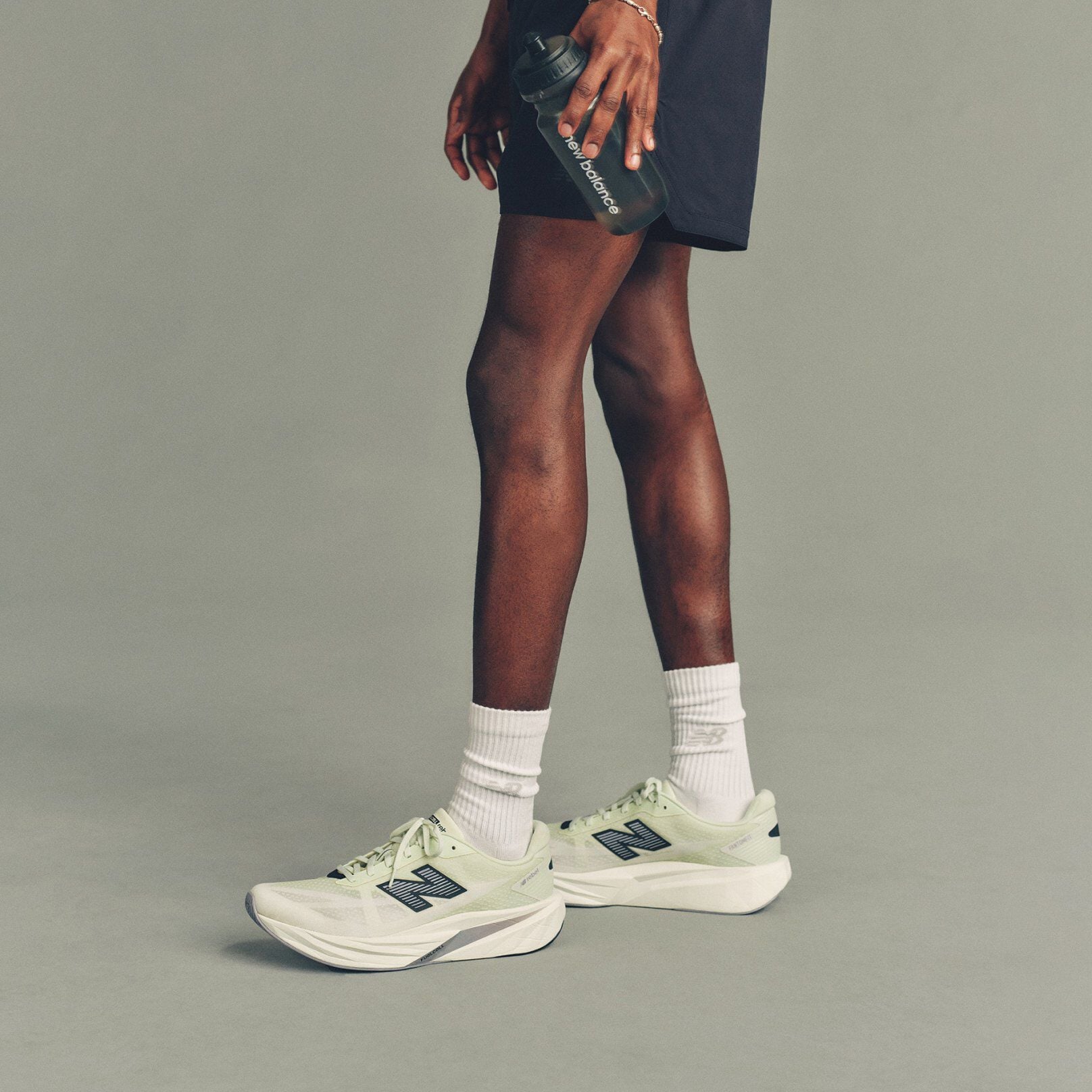 Studio image showing a person&rsquo;s lower body from mid-thigh down, standing against a smooth, light gray background.