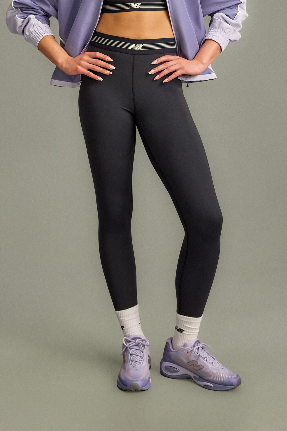 The person is wearing an olive-green matching tracksuit with a zip-up jacket and elastic-waist pants, both featuring a small New Balance logo. 