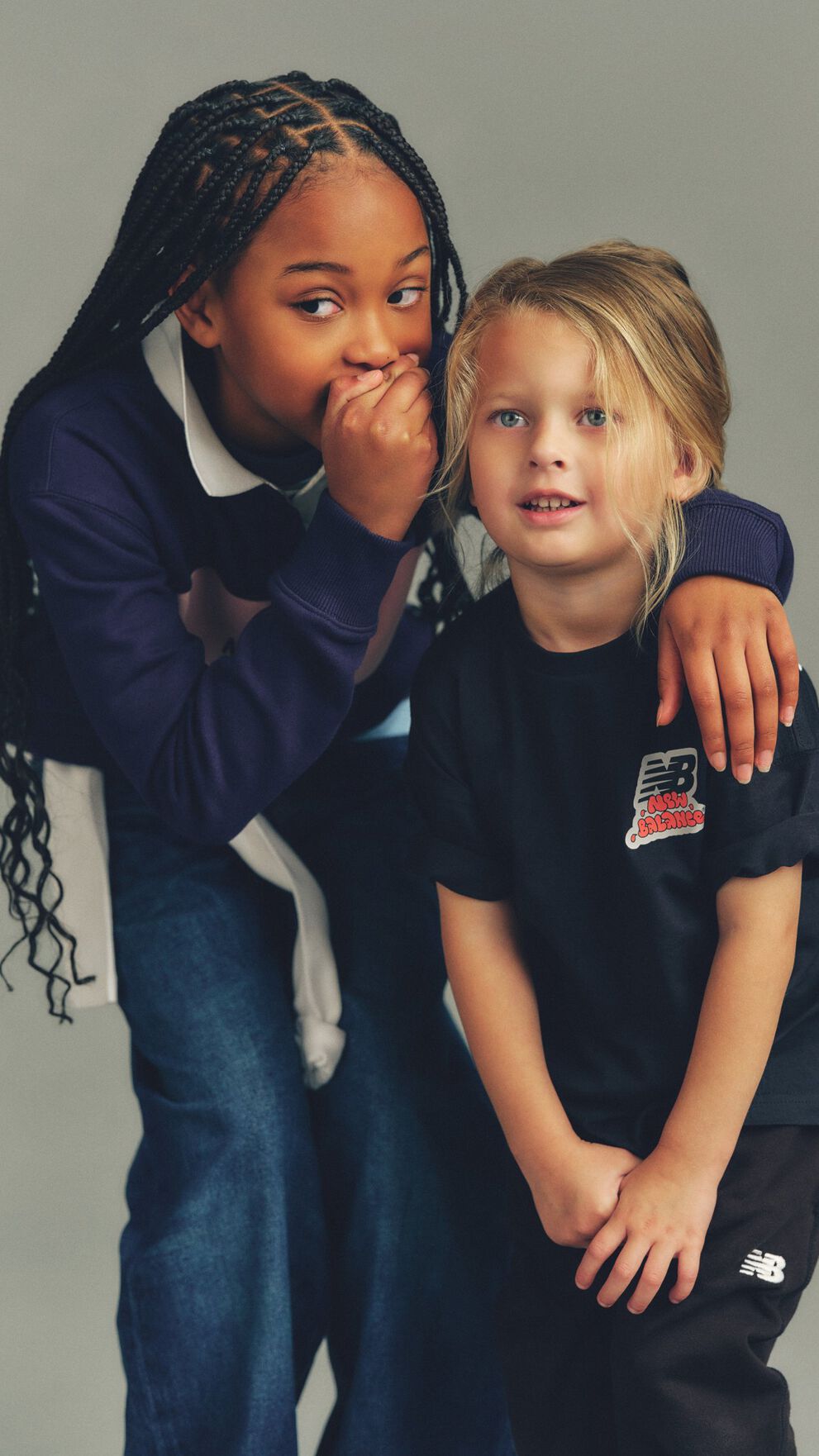 Close-up, studio-style photograph featuring two children positioned closely together against a soft, neutral gray background.