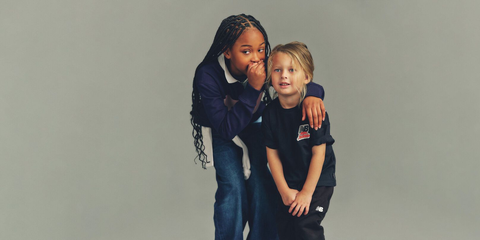 Close-up, studio-style photograph featuring two children positioned closely together against a soft, neutral gray background.