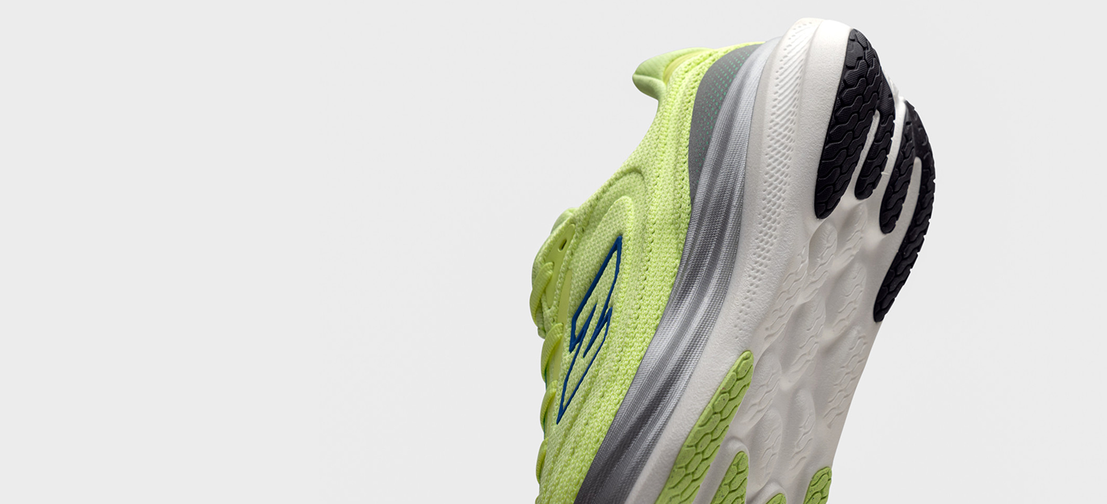 Close-up of the heel and sole of a bright yellow-green New Balance running shoe with blue logo, gray accents, and white sole featuring black tread. 