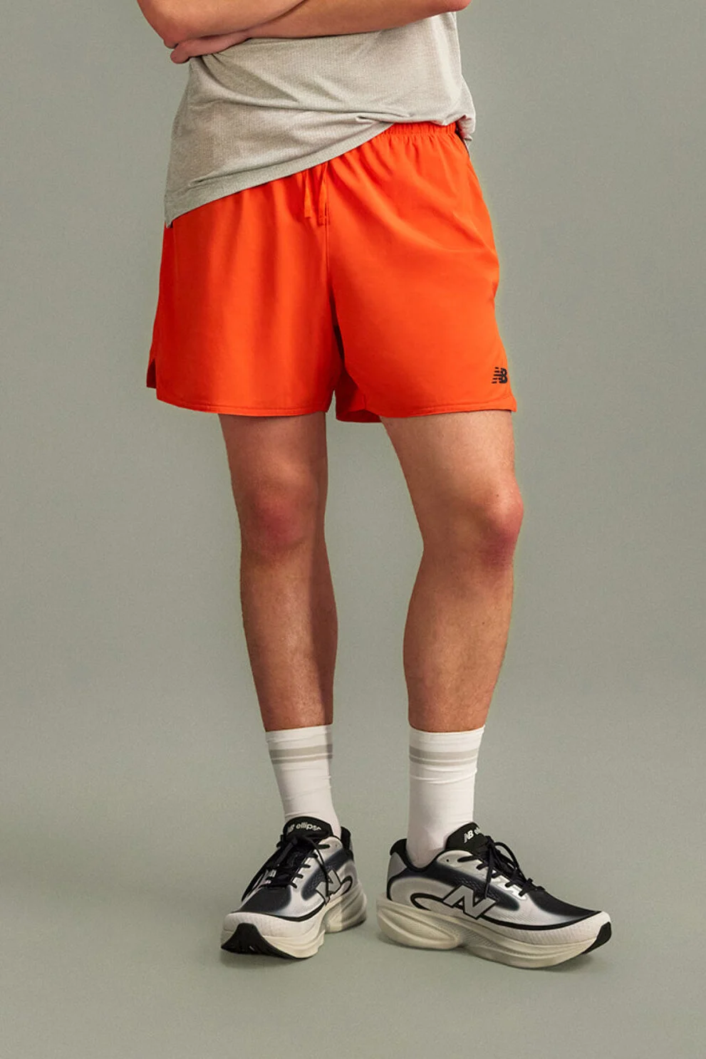 The person is wearing bright orange running shorts with a small New Balance logo near the hem and a light gray athletic T-shirt partially visible above.