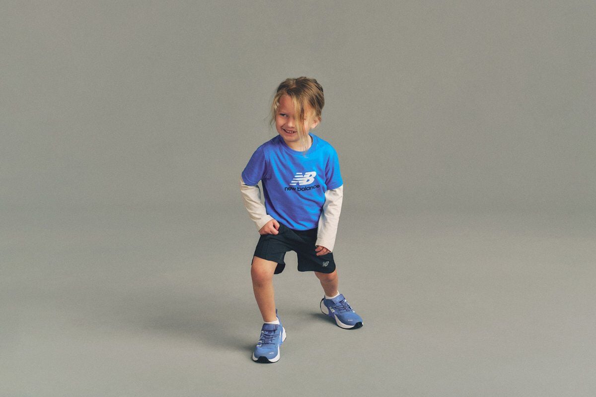 Close-up studio image of a child holding a blue, white, and purple soccer ball above the head with both hands.