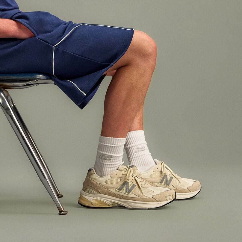 Studio image of a person seated on a metal chair, shown from mid-thigh down against a smooth, light gray background. 