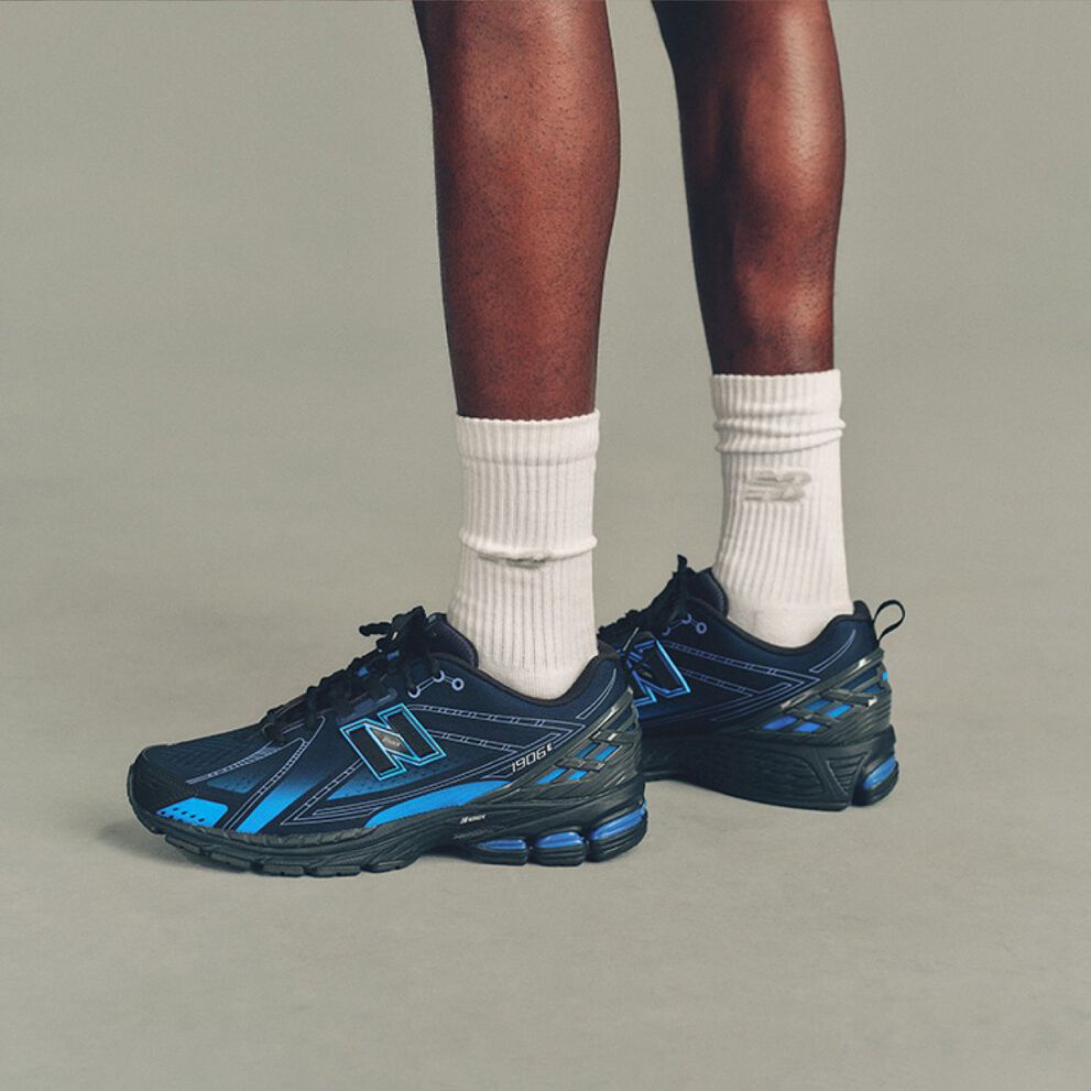 The person is wearing white ribbed crew socks and black New Balance running shoes with bright blue accents and a large outlined &ldquo;N&rdquo; logo on the sides. 